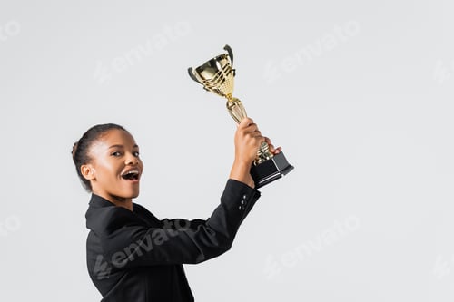 Preview: happy african american businesswoman with golden cup isolated on grey