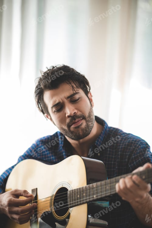 Preview: Handsome young man relaxing and enjoying playing guitar with eyes closed at home