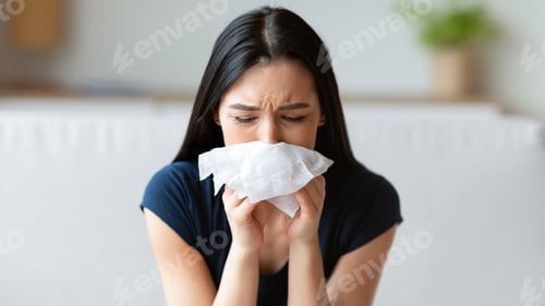 Preview: Sick Girl Sneezing Blowing Nose In Paper Tissue Sitting Indoors