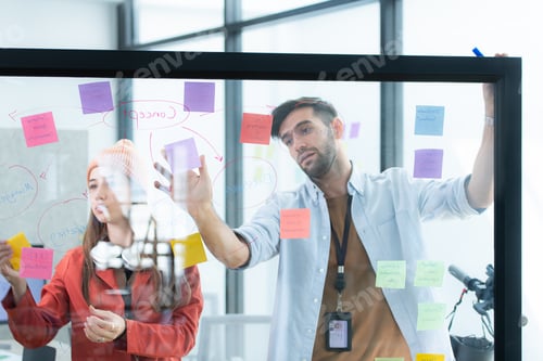 Preview: Multiethnic young business people brainstorming on a project by writing on the glass wall