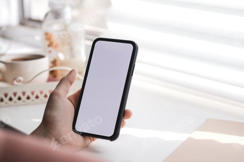 Preview: Woman uses a smartphone with a white screen, near the window at home in the morning. Mock up
