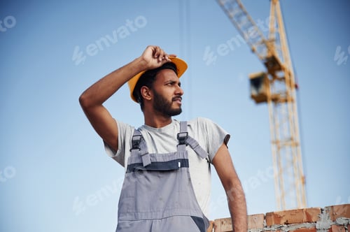 Preview: Standing against crane and blue sky. Handsome Indian man is on the construction site