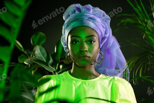 Preview: young african american woman in traditional wire head wrap under green light looking at camera