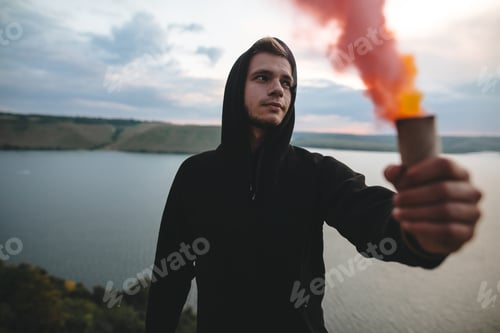 Preview: Ultras hooligan holding red smoke bomb in hand with amazing view on river