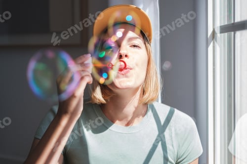 Preview: Young woman throwing soap bubbles by the window on a sunny day. Concept: lifestyle, various, fun