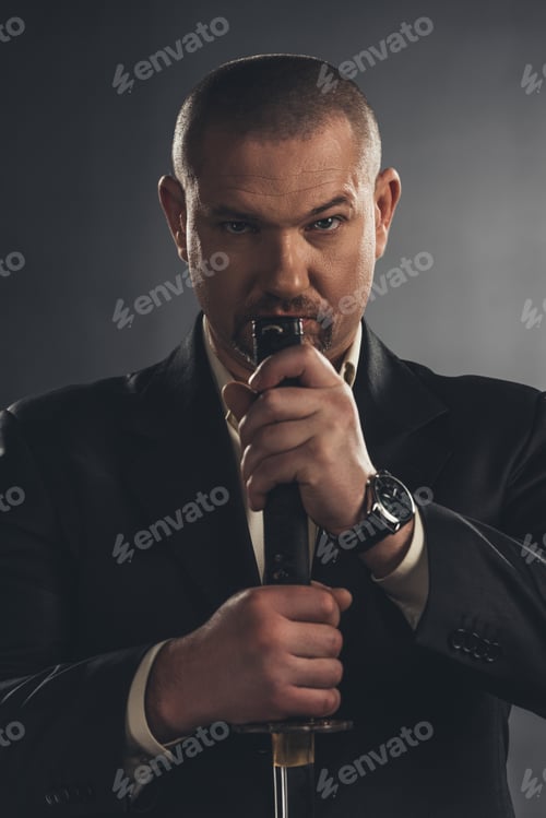 Preview: close-up portrait of adult man in suit with katana sword on black