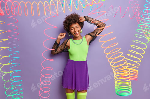 Preview: Shot of optimistic dark skinned lady has fun on hens party, dances with closed eyes, waves raised ha