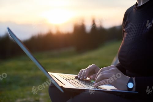 Preview: Young woman using laptop outdoors