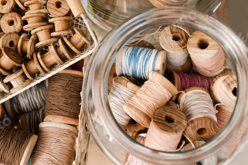 Preview: Top view on small wooden coils in a basket and big coils with colorful threads in a glass jar.