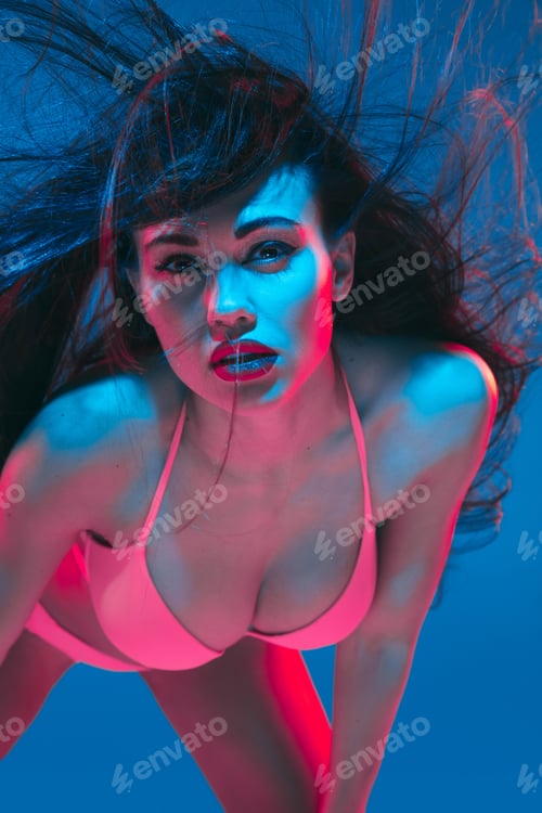 Preview: Attractive brunette model on blue studio background in neon light