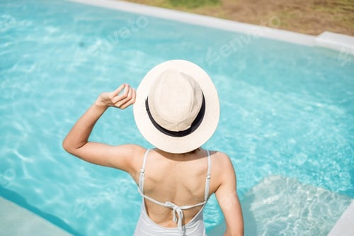 Preview: Happy woman in white swimsuit swimming in luxury pool hotel against beautiful view