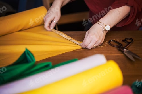 Preview: A woman using a tape measure to measure yellow fabric for cutting out.