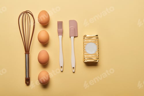 Preview: flat lay with balloon whisk, eggs, spatula, bakery brush and butter on yellow background