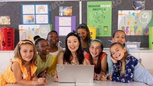 Preview: Portrait of diverse female teacher and schoolgirls using laptop in elementary school class