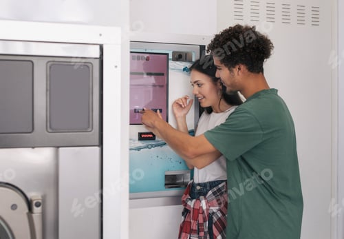 Preview: Couple Using Laundromat Paying For Washing Of Clothes At Laundrette