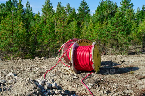 Preview: Wooden Reel with High Voltage Red Cable in Forest: Ready for Underground Power Line Installation