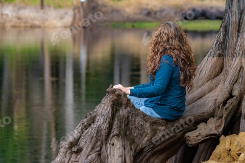 Preview: a woman sitting on the side of a tree trunk with water in the background