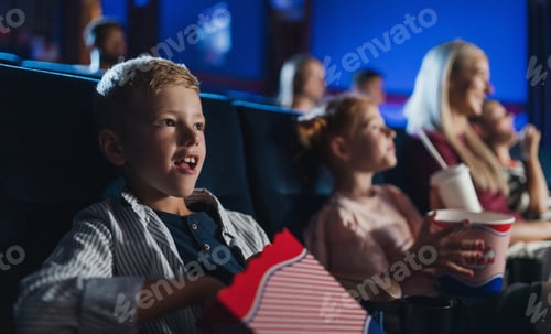 Preview: Small boy with family sitting and watching film in the cinema, eating popcorn