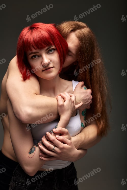 Preview: A young attractive woman with bright ruby hair in the arms of a semi-naked man with long hair. The