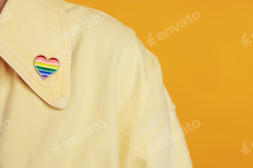 Preview: Woman with heart shaped pin in LGBT colors on orange background, closeup. Space for text