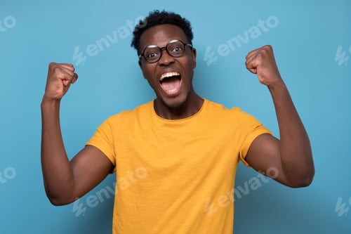Preview: Expressive african american man celebrating success raising his fists up