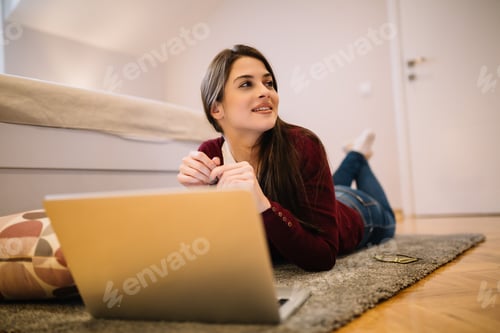 Preview: Beautiful young girl lying on floor and using laptop.