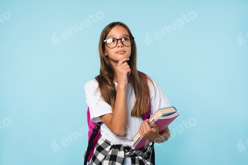 Preview: Schoolgirl thinking about school education e-learning, holding copybooks isolated in blue background