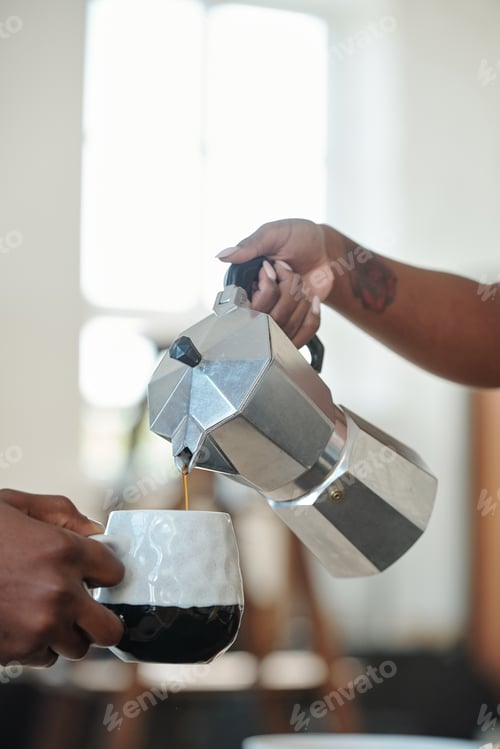 Preview: Hand of young African woman pouring coffee or tea into mug of her husband during breakfast