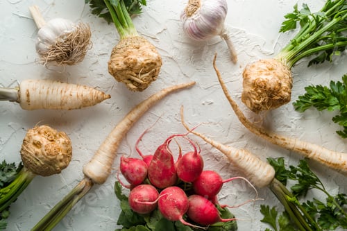 Preview: Background of celery roots, parsley, radishes with leaves and garlic on white table
