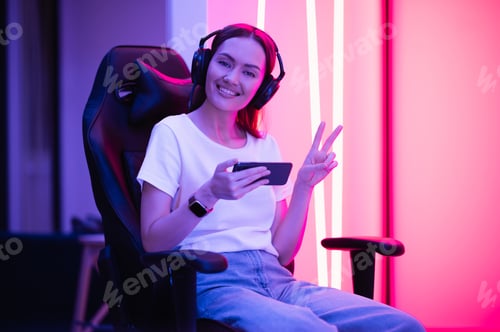 Preview: Gamer girl in white t-shirt and blue jeans holds smart phone in hands and plays game app on mobile