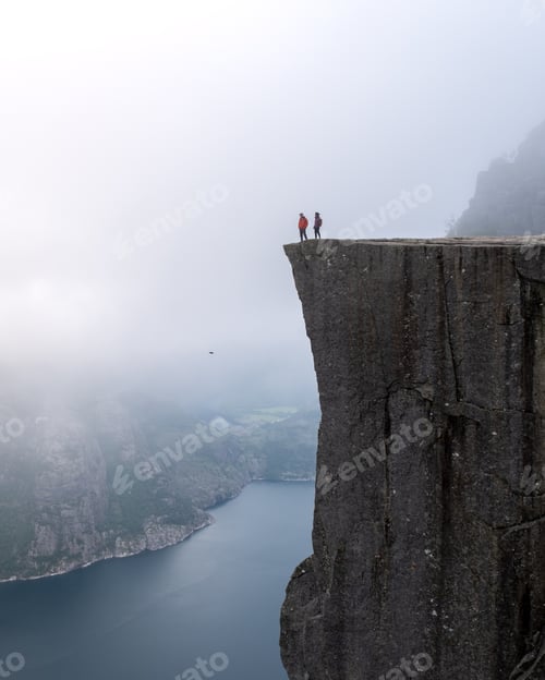 Preview: Adventurers Stand on Preikestolen Cliff Overlooking Lysefjord in Misty Norway