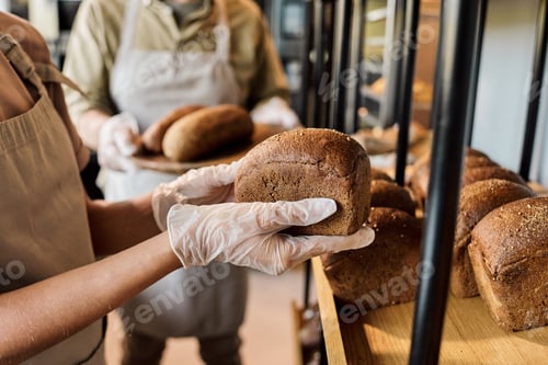 Preview: Gloved hands of young woman holding fresh loaf of bread
