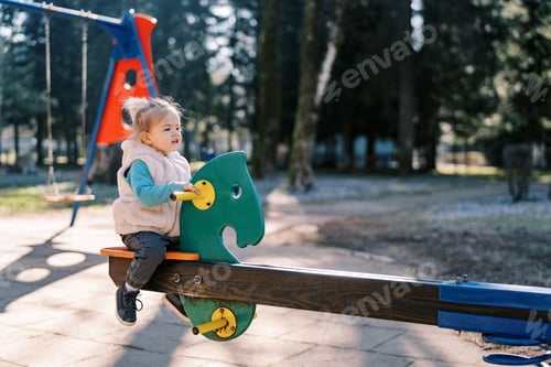 Preview: Little girl sits on a swing-balancer in the park. Side view