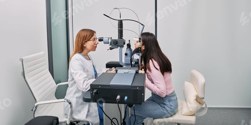 Preview: Asian woman getting eye exam at ophthalmology clinic with optometrist. Ophthalmology. Side view