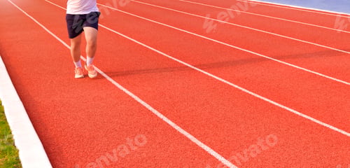 Preview: Low section of young man jogging on running track in outdoors stadium, panoramic view