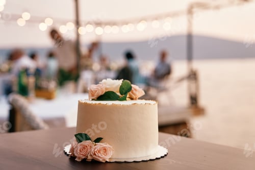 Preview: Wedding cake stands on the table against the backdrop of guests sitting at a table on the seashore