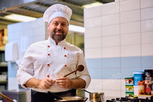 Preview: Smiling mature chef cooking in a restaurant and looking at camera.