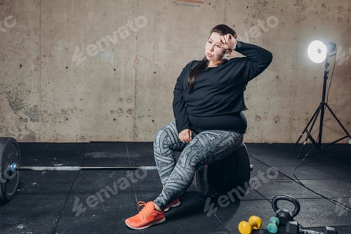 Preview: tired fat girl with hand on her forehead sitting at gym