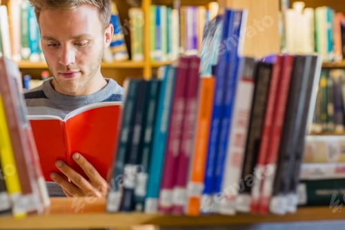 Preview: Young Male Student Reading A Book Amid Bookshelves In The College Library