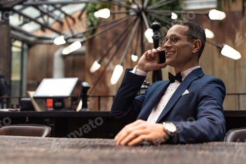 Preview: handsome adult man in suit talking by phone at restaurant