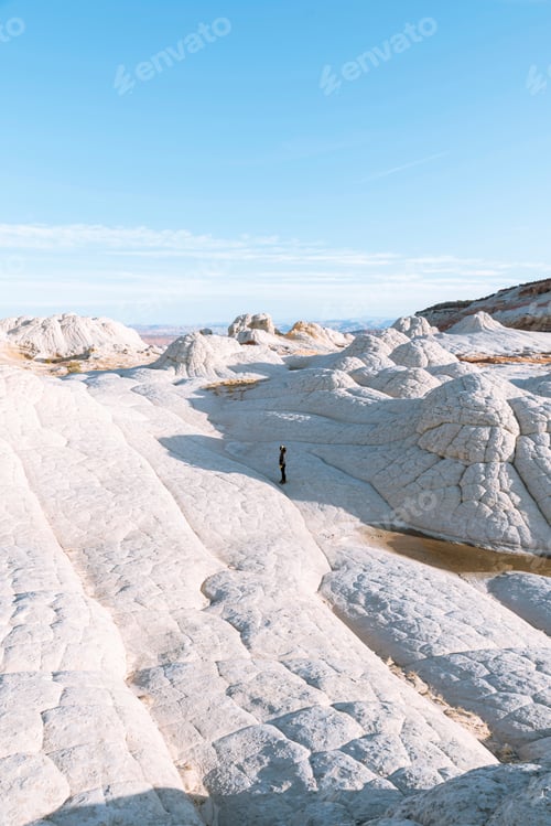 Preview: A lone explorer amidst vast white rock formations under a clear blue sky.