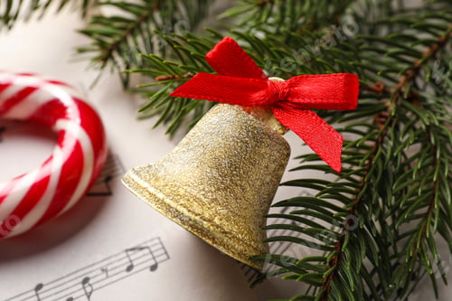Preview: Golden shiny bell with red bow and fir branches on music sheet, closeup. Christmas decoration