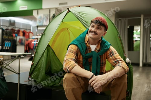 Preview: Happy smiling hipster man bicyclist sitting nearby travel camp tent in store