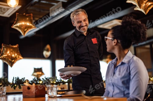 Preview: Smiling Waiter Serving an African-American Woman at Festive Restaurant with Decorations