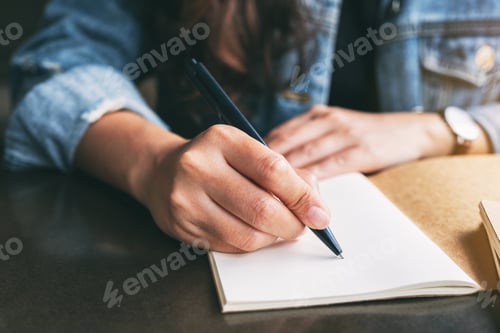 Preview: Closeup image of a woman writing on a blank notebook on the table