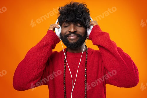 Preview: African american man joyfully listening to music against orange background