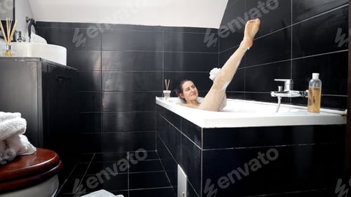 Preview: Sexy woman washing long legs in black bathroom with sponge. Female hygiene, relaxing in bathroom