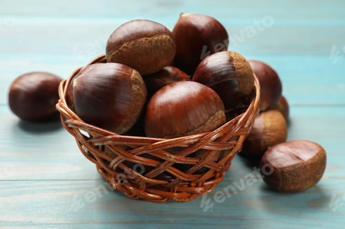 Preview: Wicker bowl with roasted edible sweet chestnuts on light blue wooden table, closeup