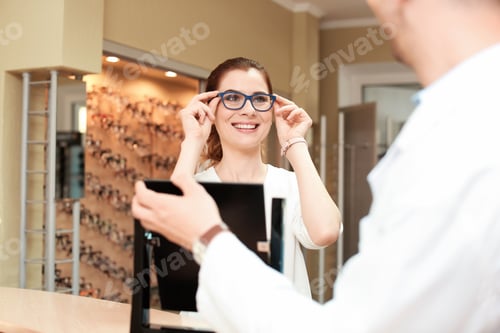 Preview: Male ophthalmologist helping woman to choose glasses in optical store