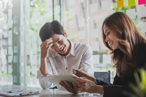 Preview: Two young asian business people using tablet working together on business plan in the office.